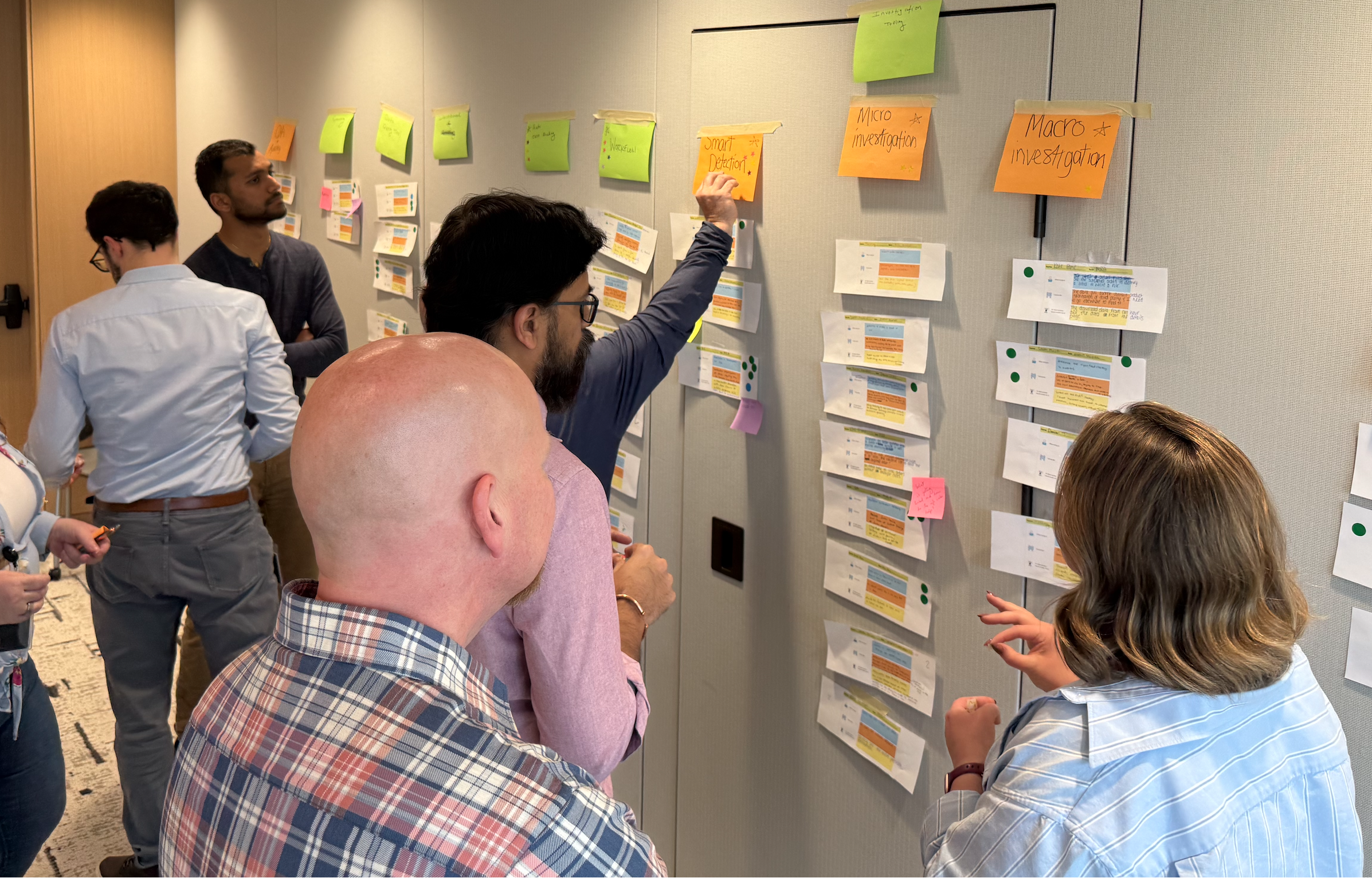 Cross-functional team clustered around printed journey maps and screens during a design sprint